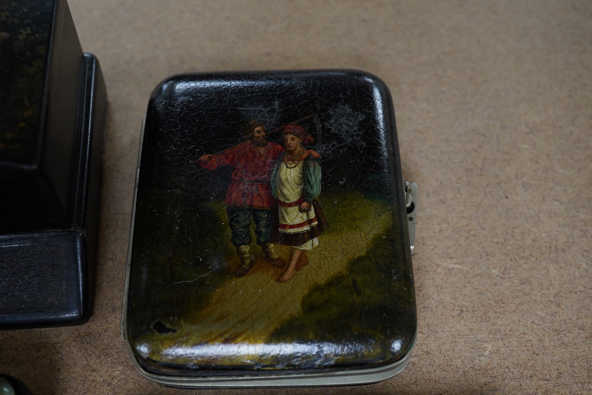 Three Russian lacquer cigarette cases, late 19th/early 20th century, one decorated with a troika scene and a match strike, 11cm wide. Condition - good